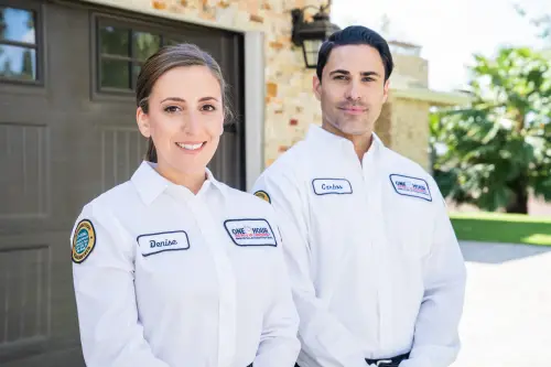 One Hour Air Conditioning Techs, Denise and Carlos, in front of a Miami home's garage